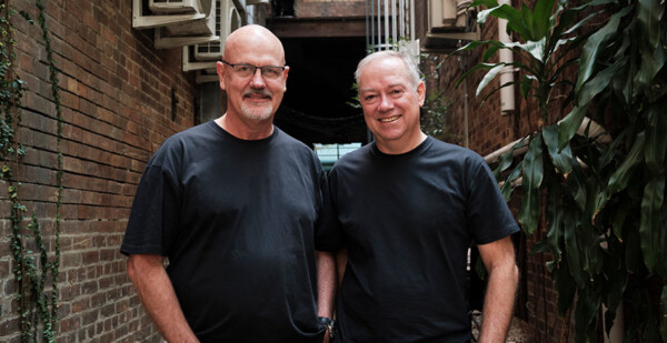 Two smiling men in black shirts in outdoor setting