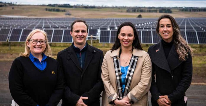 Executives from Flow Power and ACEN Australia pose for photo standing in front of solar panels at New England Solar Farm