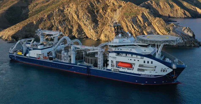 Aerial shot of Prysmian's cable-laying vessel the Leonardo Da Vinci in a calm ocean inlet with mountains behind it