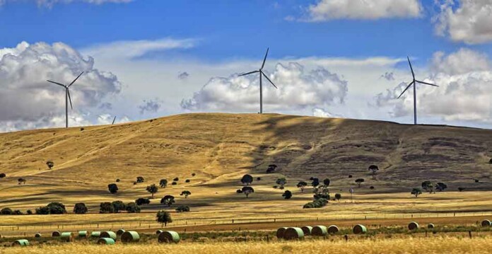 Wind farm in Australia with rolling green hills and blue cloudy sky above